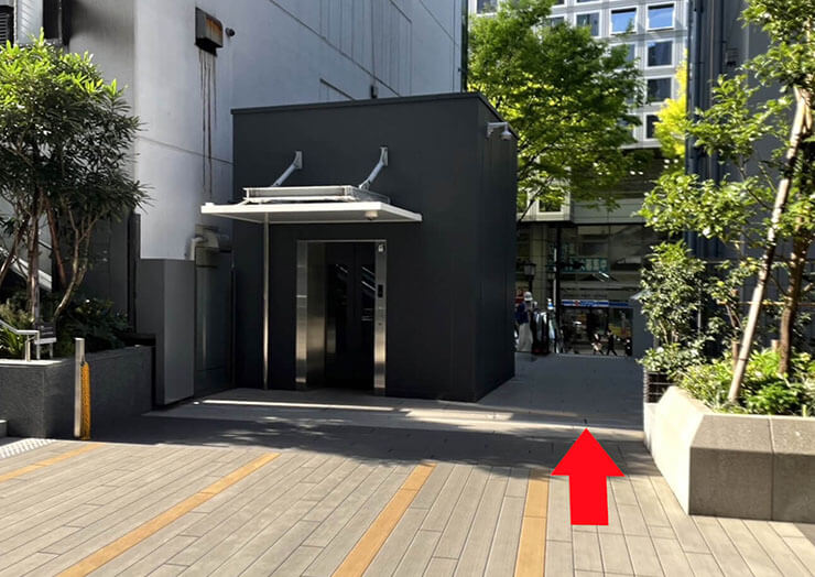 画像：手前から、左手に見えるエレベータ昇降口の横の道に向かって、赤い矢印が表示されています。