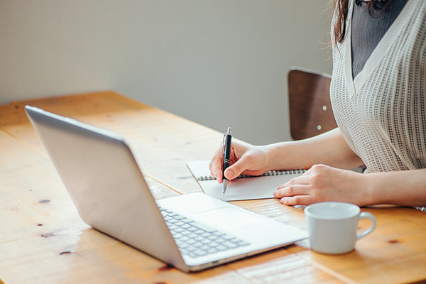 パソコンを見ながらノートをとっている女性のイメージ画像