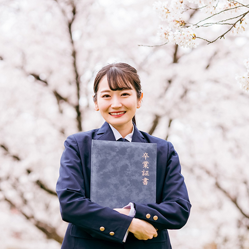 桜の下で卒業証書を持つ女子生徒