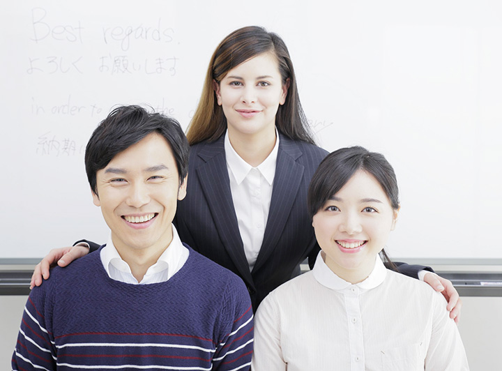 笑顔の生徒2人と、二人の後ろで生徒の肩を寄せ微笑む講師の写真