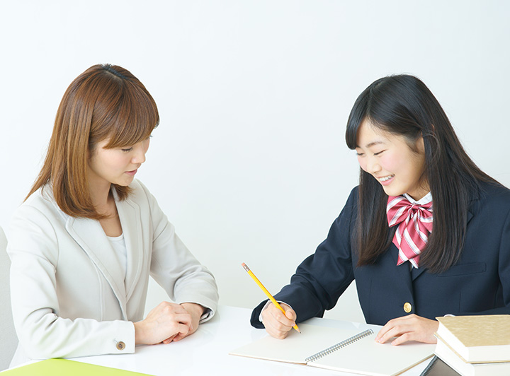 講師からの指導を笑顔でノートにつづる女子高校生のイメージ画像