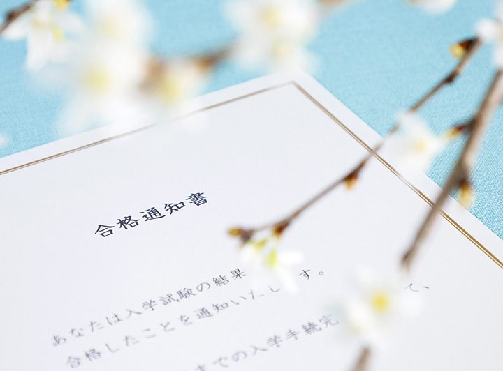 水色のテーブルに置かれた白い合格通知書。手前には桜の咲いた枝が花を添えている。