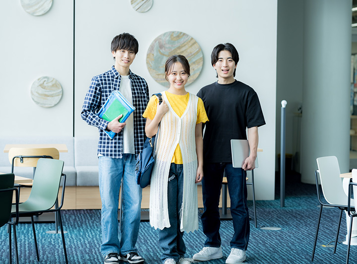 大学のキャンパスで笑顔で立っている3人の大学生