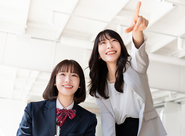 正面を指さす講師と、さした方法を笑顔で見つめる高校生