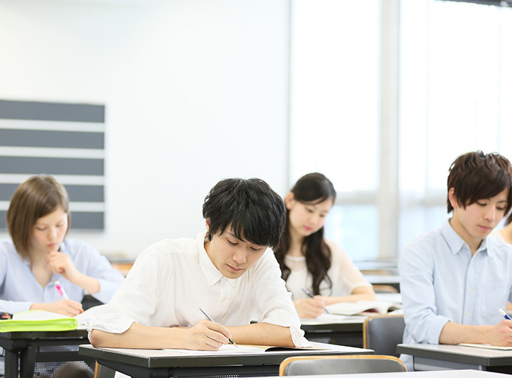 テストを受けている人のイメージ画像。男性が教室で紙の試験を受験している。