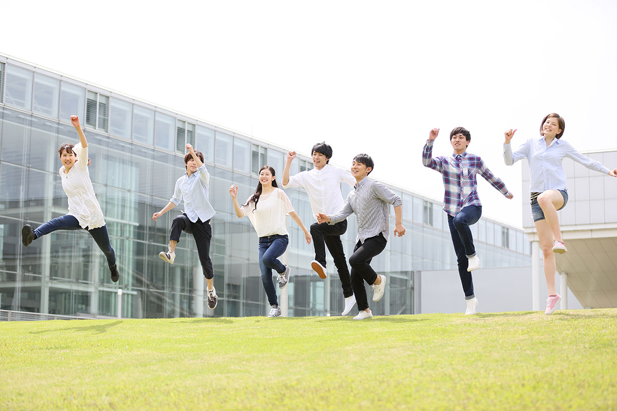 【本文用】芝生の上でジャンプする大学生グループ