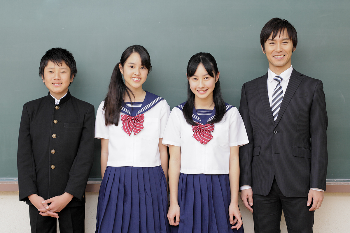 【本文用】黒板の前に笑顔で立つ中学生と教師