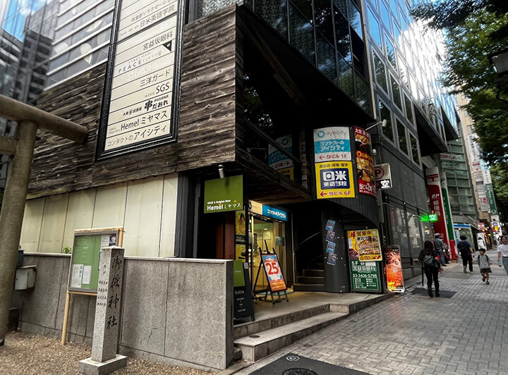 画像：神社の隣のビル写真。日米英語学院渋谷校の看板があります。
