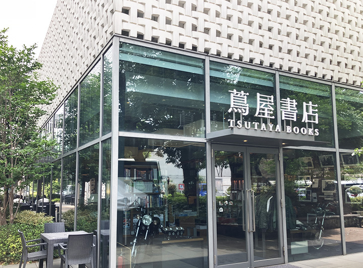 蔦屋書店入り口の写真。ガラス張りの壁で中の様子が外からうかがえる。周囲には街路樹があり落ち着いた空間である。