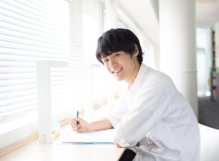 窓際で勉強している学生がこちらを振り返り笑顔を向けてくれている