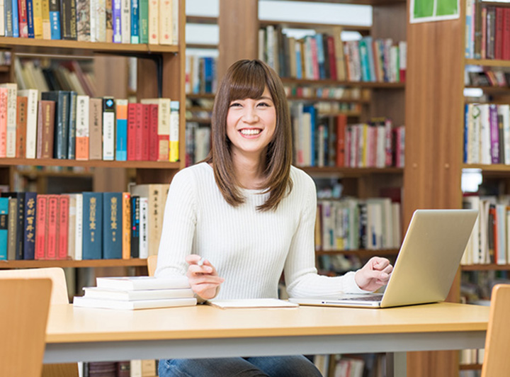 図書館で学習する女性。話しかけられ、笑顔で応答している。