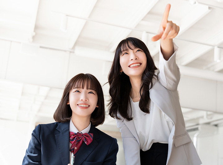 前を指さす女性講師とそれを見つめる女子生徒