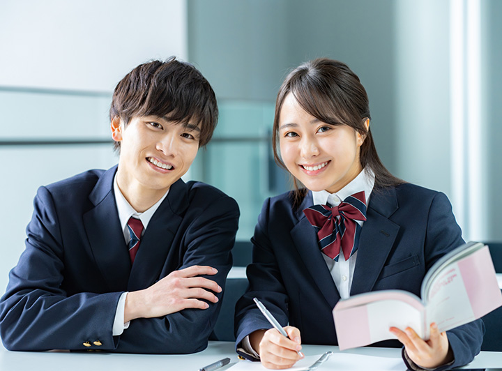 海外のオフィスシーンの写真。座っている上司を囲んで話をするビジネスマンと、腕を組んで笑顔の女性。