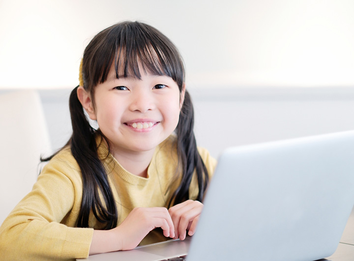 パソコンの前で笑顔で笑う小学生女子