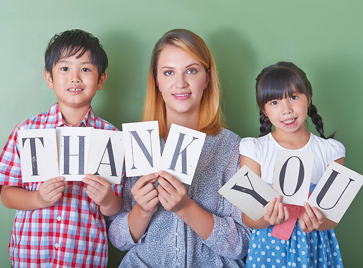 ネイティブ講師の両脇に小学生が立っている。3人で「thankyou」という紙を掲げている。