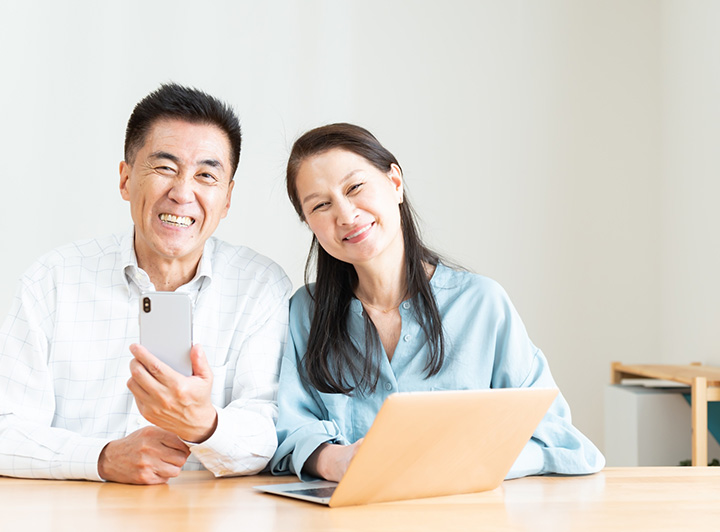 パソコンとスマホを見ながら微笑みあう熟年夫婦