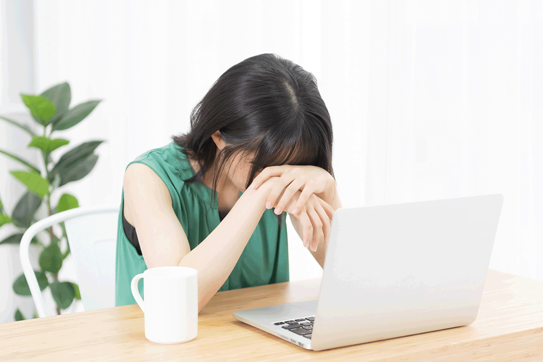 ノートパソコンの前で頭をうなだれて考える女性
